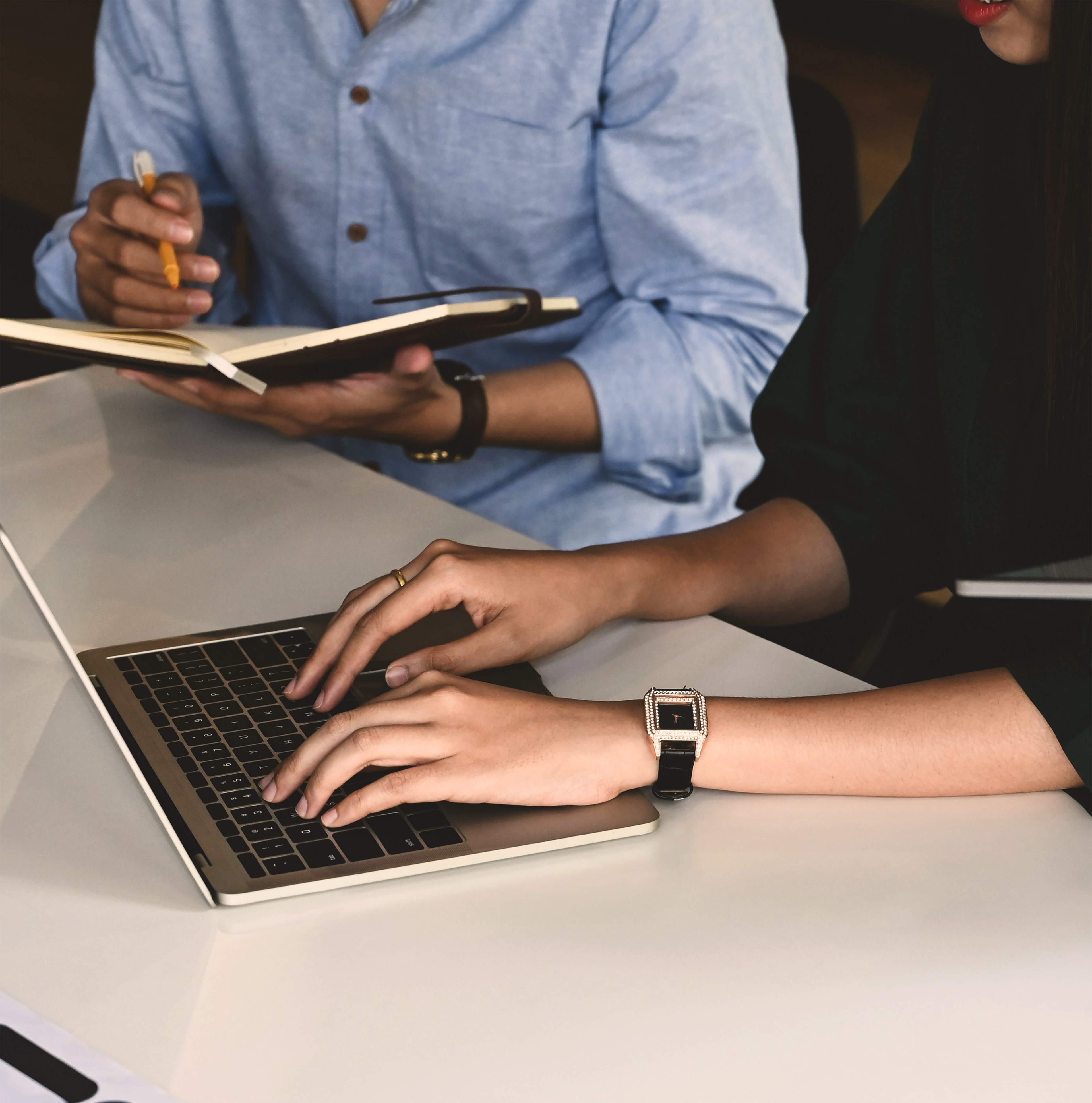 Two people collaborating at a desk with a laptop and notebook at MODE