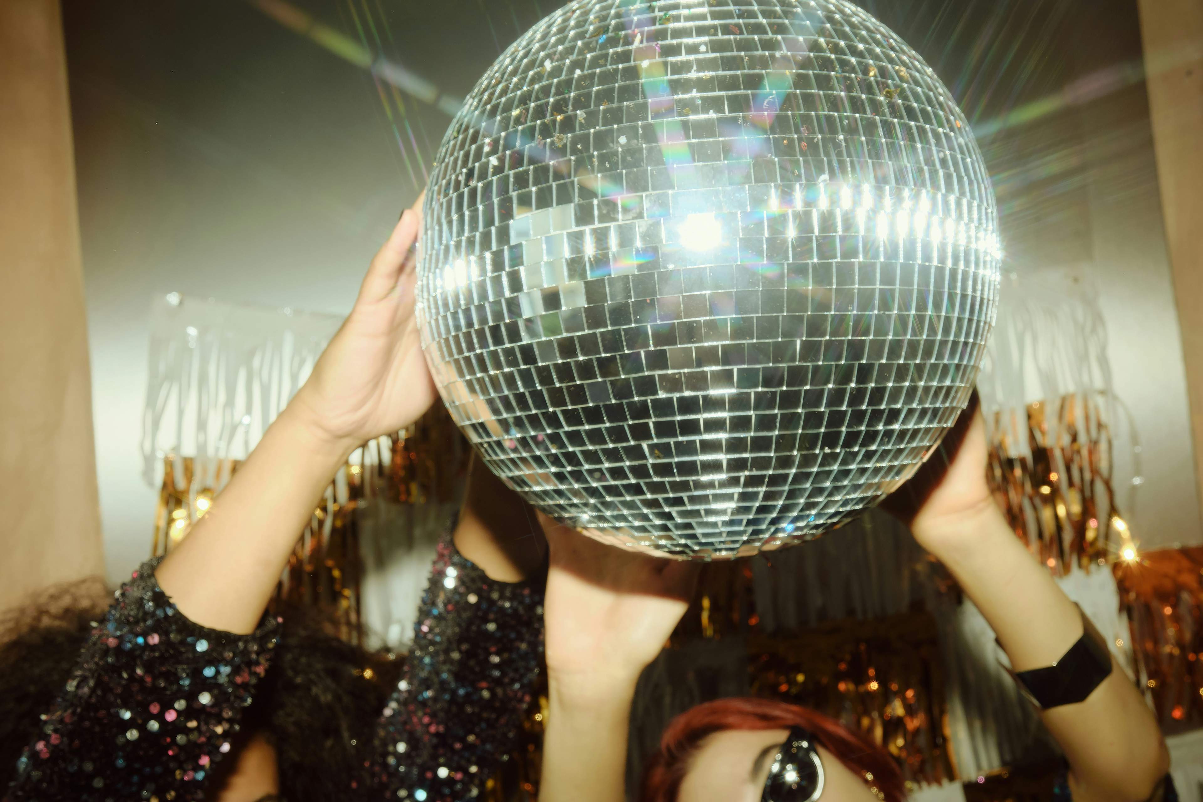Guests holding a disco ball at a MODE Social event under gold tinsel
